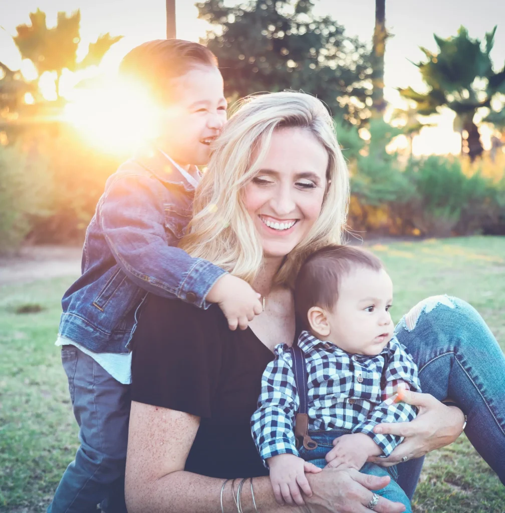 Une mère souriante assise dans un parc, entourée de ses deux jeunes enfants.